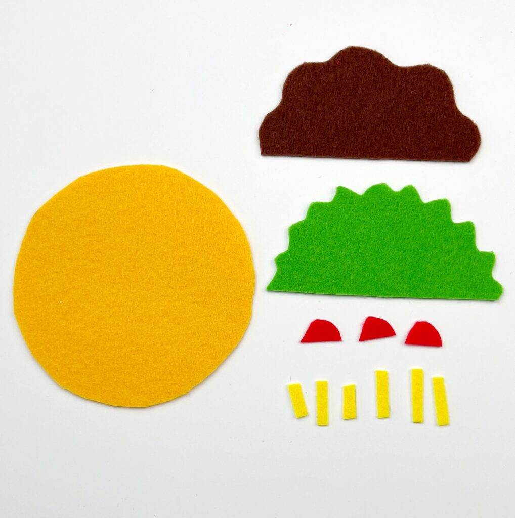 Completed taco ornament pieces cut from felt - the yellow circle is the tortilla, there is a curved brown piece for meat, jagged green lettuce, small red pieces for tomato, and little rectangles that are grated cheese