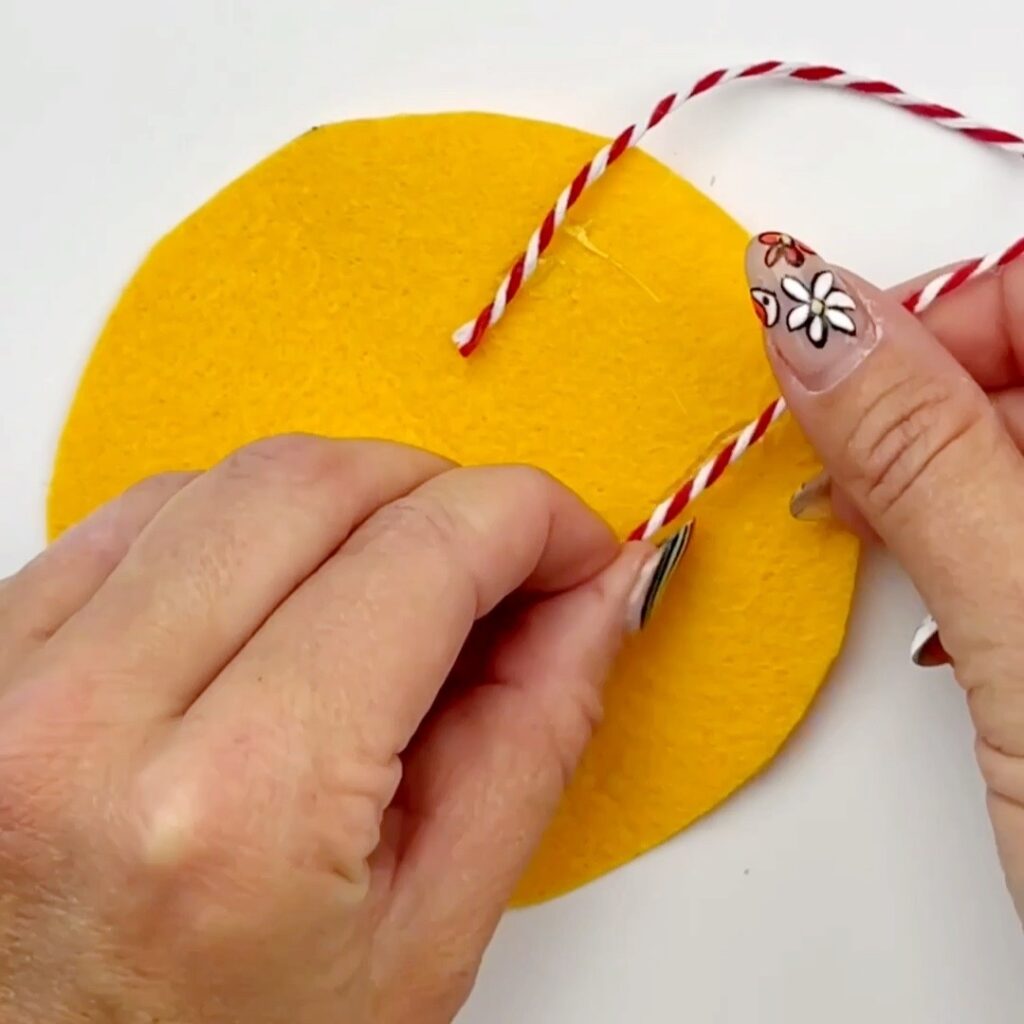 Glueing a piece of twine to the yellow felt circle. A loop sticks out and the ends are glued down so the ornament can hang