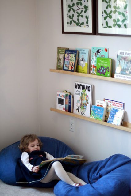 Toddler looking at book while laying on a comfortable bean bag chair in a reading corner